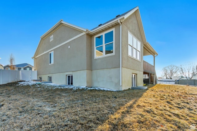 rear view of house featuring fence, stairway, and stucco siding