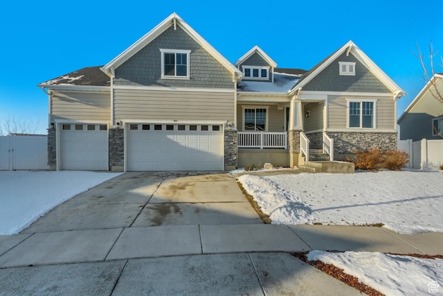 view of front facade with a porch, stone siding, concrete driveway, fence, and an attached garage