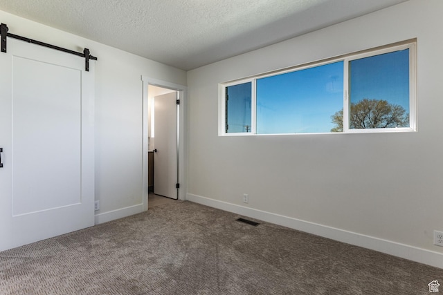 unfurnished bedroom with a textured ceiling, a barn door, baseboards, visible vents, and carpet