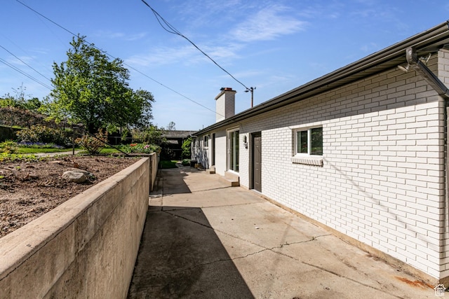 view of property exterior with brick siding, a patio area, and a chimney