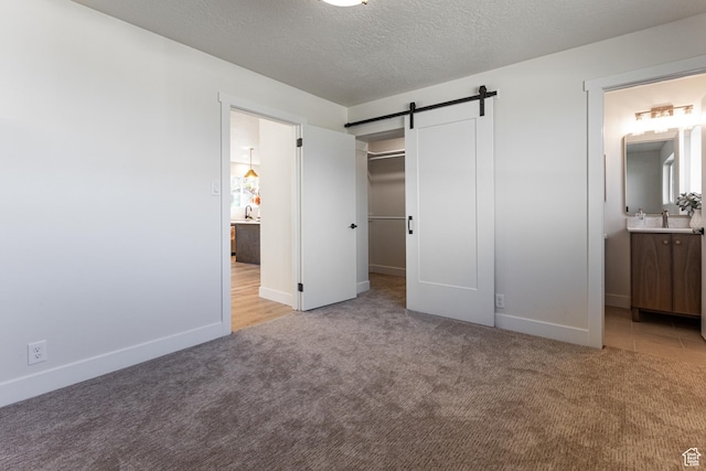 unfurnished bedroom with a walk in closet, a barn door, light carpet, and baseboards