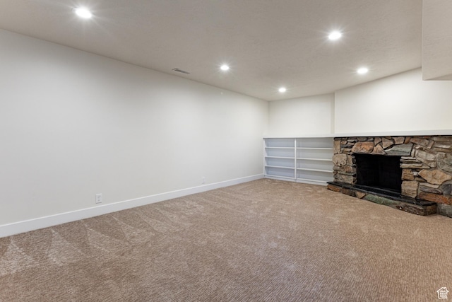 finished below grade area with carpet flooring, visible vents, baseboards, recessed lighting, and a stone fireplace