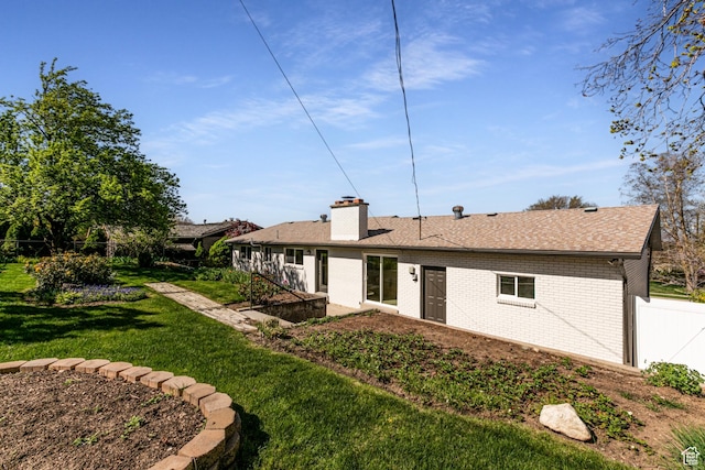 back of house featuring a chimney, a lawn, a shingled roof, fence, and brick siding