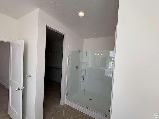 bathroom featuring a walk in closet, baseboards, tile patterned floors, and a stall shower