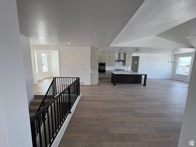 corridor featuring baseboards, a wealth of natural light, a textured ceiling, and light wood-style flooring