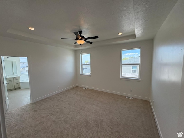 empty room with a raised ceiling, visible vents, a ceiling fan, baseboards, and light colored carpet