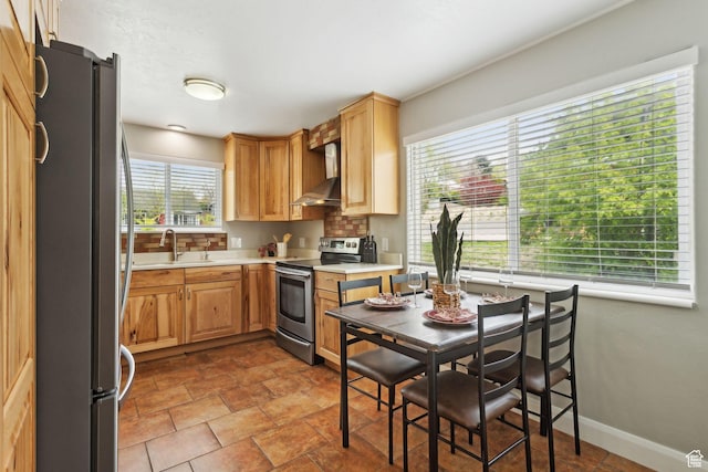 kitchen featuring a sink, appliances with stainless steel finishes, light countertops, baseboards, and wall chimney exhaust hood