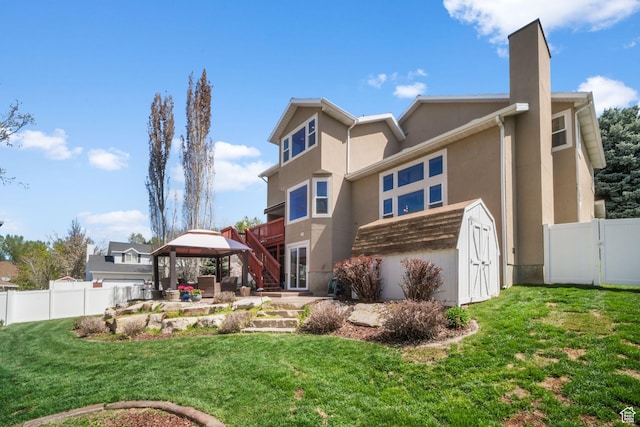 rear view of property featuring a gazebo, a yard, stucco siding, and fence