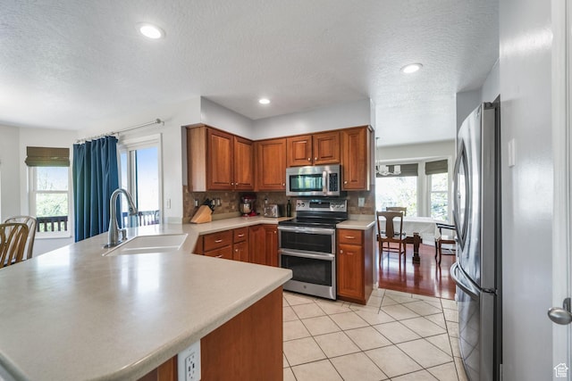 kitchen with a textured ceiling, a sink, brown cabinetry, stainless steel appliances, and a peninsula