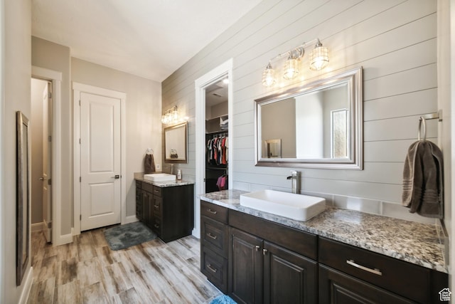 full bathroom with two vanities, wood finished floors, a sink, and a spacious closet