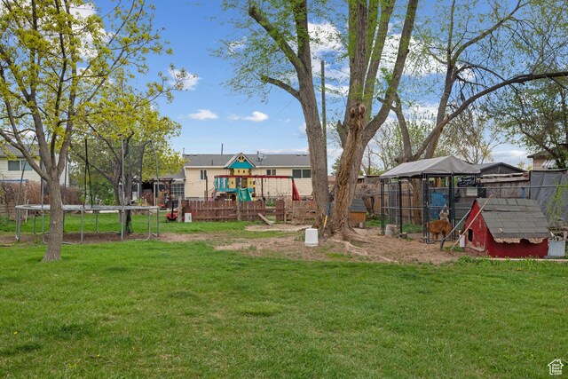 view of yard featuring a playground, fence, exterior structure, an outbuilding, and a trampoline