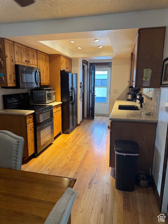 75 S Cooley St W, Grantsville, UT 84029 - kitchen featuring a raised ceiling, a sink, light wood-style flooring, black appliances, and brown cabinetry