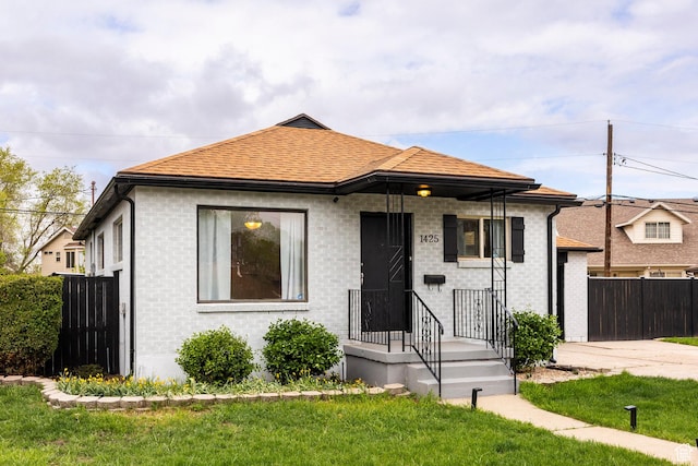 bungalow-style house featuring brick siding, a front lawn, fence, and a shingled roof