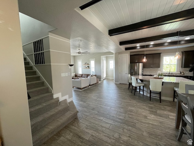 living area with baseboards, stairs, ceiling fan, beam ceiling, and dark wood-type flooring