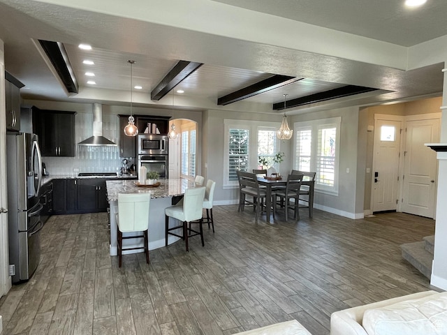 kitchen with light wood-style floors, appliances with stainless steel finishes, wall chimney range hood, and decorative backsplash