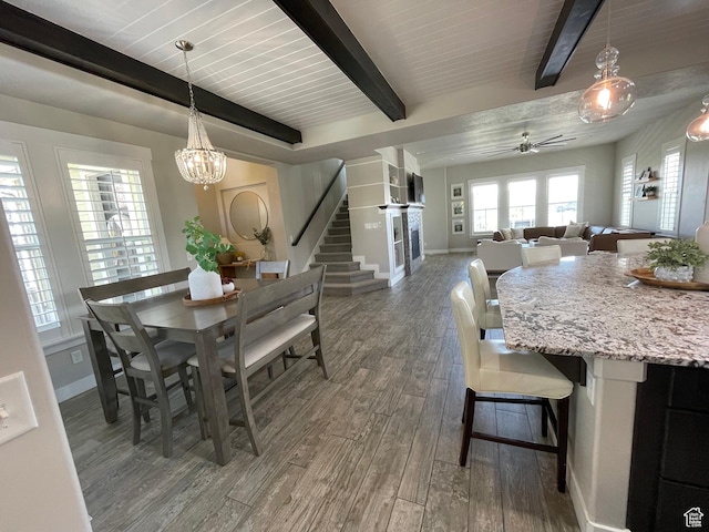 dining room with beamed ceiling, stairway, baseboards, wood finished floors, and ceiling fan with notable chandelier