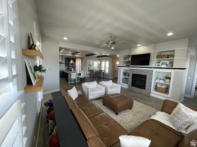 living room featuring ceiling fan, built in features, a tiled fireplace, baseboards, and recessed lighting