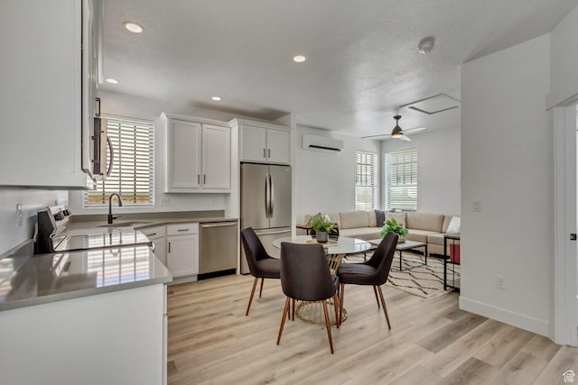 kitchen featuring white cabinets, light wood-style flooring, a sink, a wall mounted AC, and appliances with stainless steel finishes