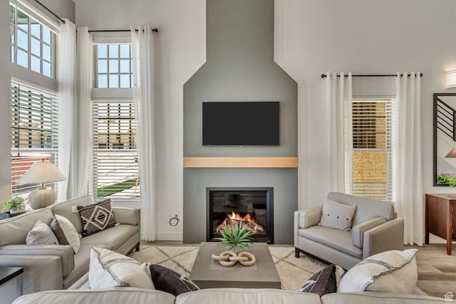 living room featuring a towering ceiling, a glass covered fireplace, and wood finished floors