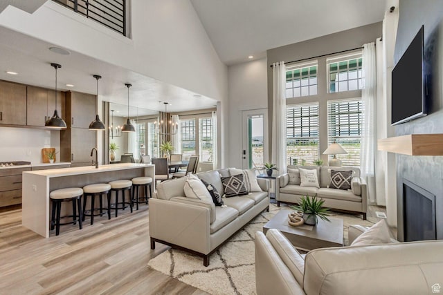 living room featuring light wood finished floors, an inviting chandelier, recessed lighting, high vaulted ceiling, and a high end fireplace