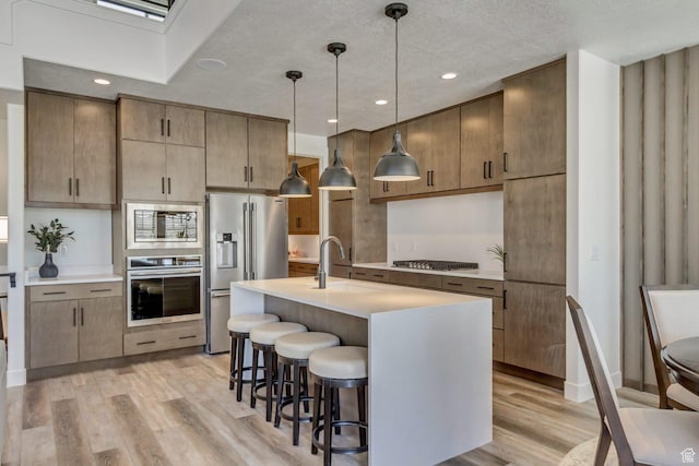 kitchen with a sink, light countertops, a breakfast bar area, stainless steel appliances, and light wood-style flooring