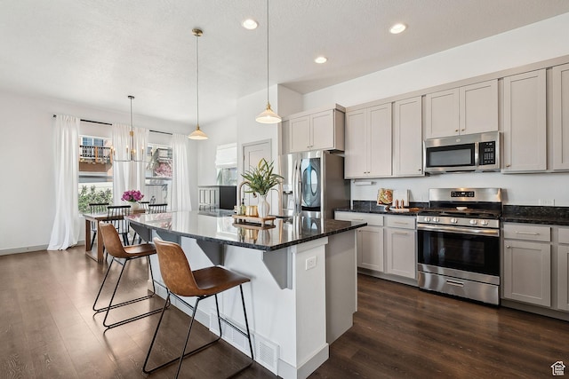 kitchen with a kitchen breakfast bar, stainless steel appliances, dark stone countertops, dark wood-type flooring, and a kitchen island