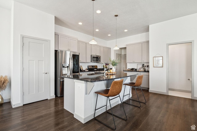 kitchen featuring stainless steel appliances, a sink, dark wood finished floors, a kitchen bar, and an island with sink