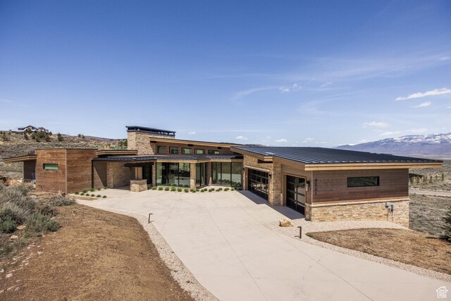 view of front facade with an attached garage, a standing seam roof, driveway, stone siding, and a mountain view