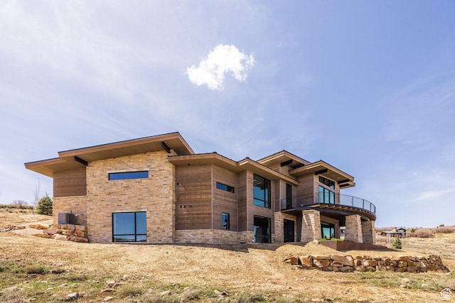 view of home's exterior with stone siding, a balcony, and cooling unit