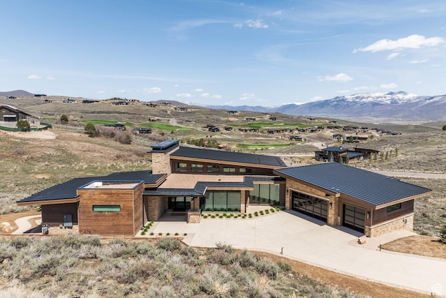 prairie-style house featuring a standing seam roof, driveway, stone siding, a mountain view, and metal roof