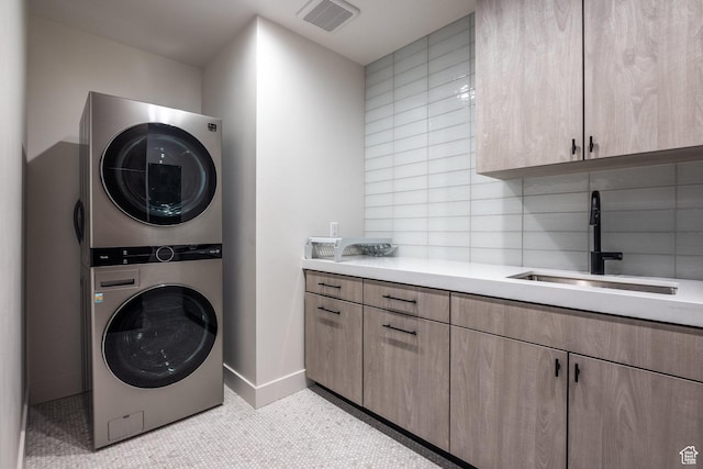 laundry room with a sink, cabinet space, stacked washer / drying machine, baseboards, and visible vents