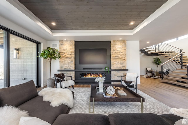 living area with wood finished floors, stairway, a stone fireplace, and a raised ceiling