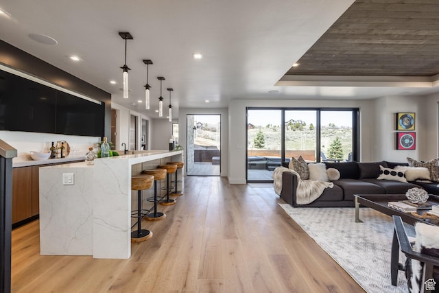 living room featuring recessed lighting, a raised ceiling, and light wood finished floors