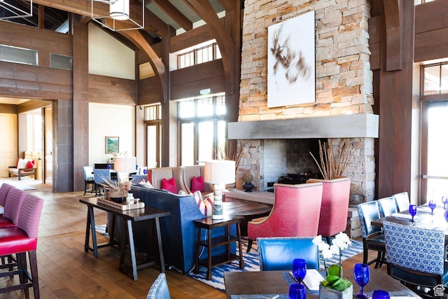 living area featuring hardwood / wood-style floors, a stone fireplace, a high ceiling, and beamed ceiling