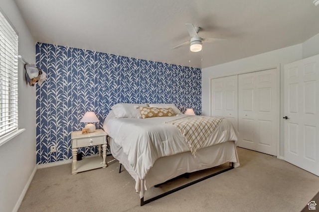 bedroom featuring baseboards, an accent wall, light colored carpet, wallpapered walls, and a closet