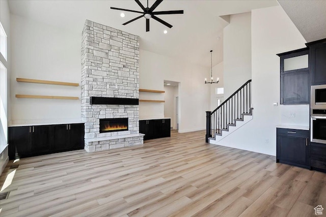 2649 N 3975 W, Plain City, UT 84404 - unfurnished living room featuring light wood-style floors, ceiling fan with notable chandelier, stairway, a stone fireplace, and high vaulted ceiling