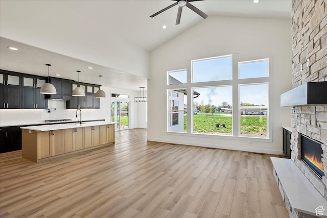 2649 N 3975 W, Plain City, UT 84404 - unfurnished living room with a sink, light wood-style floors, ceiling fan, a stone fireplace, and high vaulted ceiling