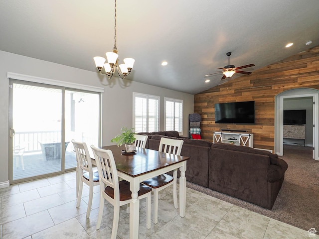 dining space featuring wood walls, vaulted ceiling, light tile patterned floors, arched walkways, and ceiling fan with notable chandelier