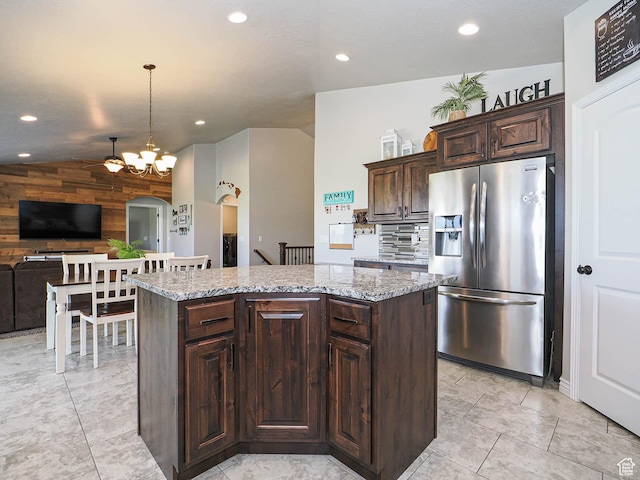kitchen with dark brown cabinetry, recessed lighting, stainless steel fridge with ice dispenser, wooden walls, and a kitchen island