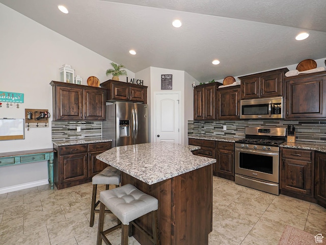 kitchen with dark brown cabinets, decorative backsplash, appliances with stainless steel finishes, a kitchen island, and a breakfast bar area