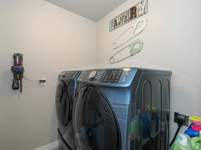 washroom with washing machine and dryer, a textured ceiling, baseboards, and laundry area