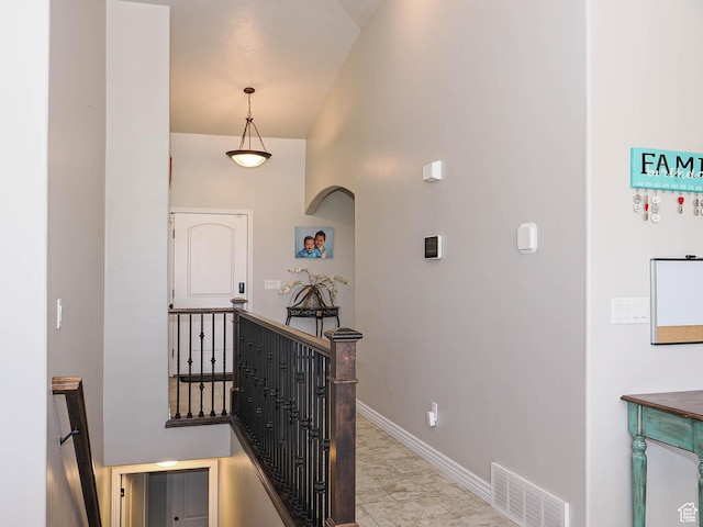hallway featuring baseboards, visible vents, a high ceiling, and an upstairs landing