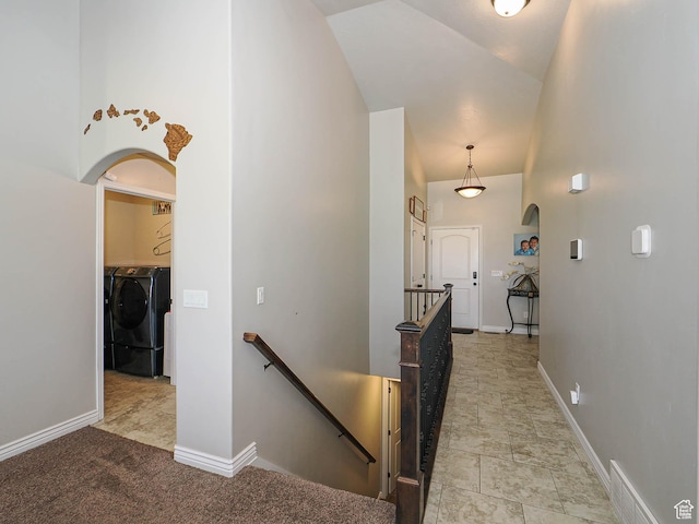 hall featuring an upstairs landing, washing machine and dryer, arched walkways, baseboards, and high vaulted ceiling