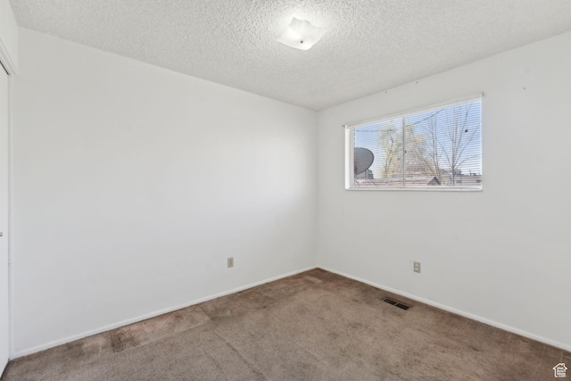 empty room with visible vents, a textured ceiling, carpet, and baseboards