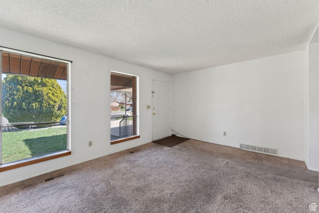 carpeted empty room featuring a textured ceiling and visible vents