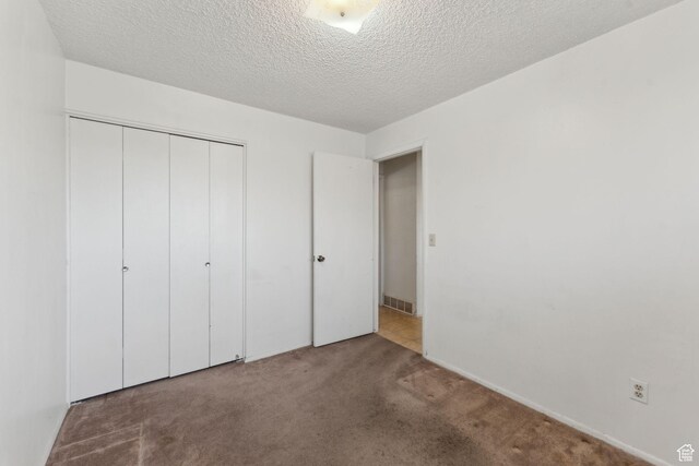 unfurnished bedroom featuring visible vents, a textured ceiling, carpet, and a closet