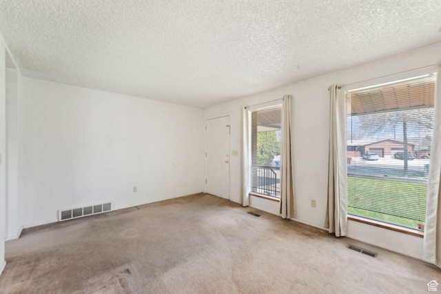 carpeted empty room featuring a textured ceiling and visible vents