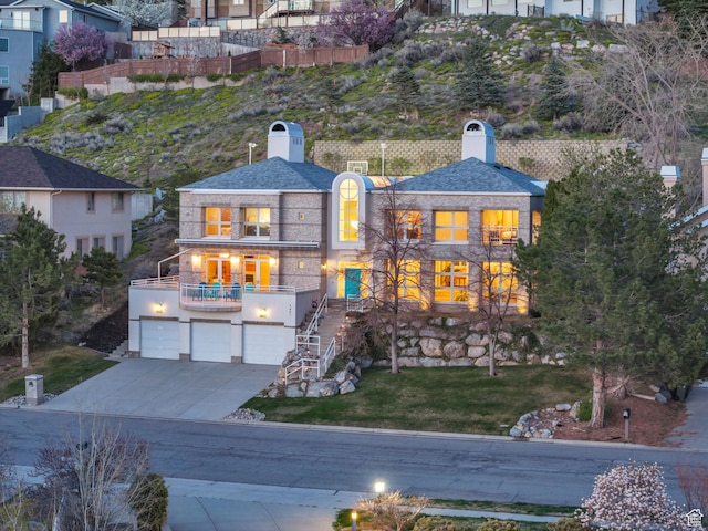 view of front of home featuring driveway, a chimney, an attached garage, stairs, and a balcony