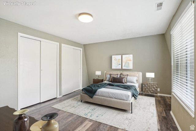 bedroom featuring two closets, dark wood-style floors, and baseboards