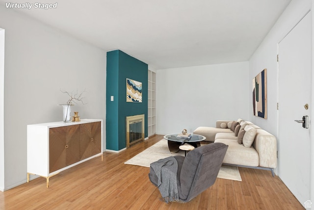 living room featuring light wood-style flooring, built in features, and a fireplace